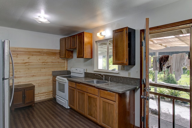 kitchen with stainless steel fridge, dark wood-type flooring, sink, wooden walls, and white electric stove