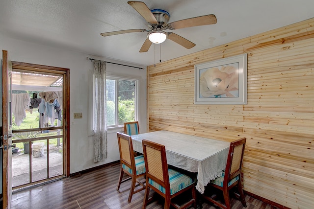 dining room with dark wood-type flooring, ceiling fan, and wood walls