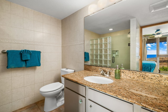 bathroom with tile patterned floors, vanity, a shower with door, tile walls, and toilet