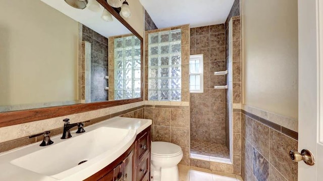 bathroom featuring tile patterned floors, toilet, tiled shower, vanity, and tile walls