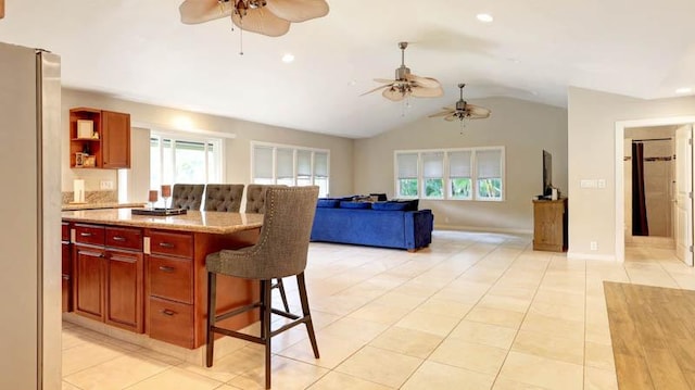 kitchen with a kitchen breakfast bar, light tile patterned floors, vaulted ceiling, and stainless steel refrigerator