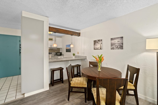 dining area featuring beamed ceiling, dark wood-type flooring, and a textured ceiling