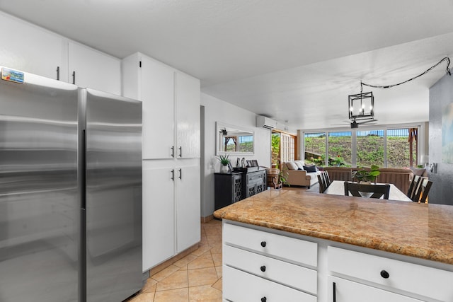 kitchen with white cabinetry, a wall unit AC, stainless steel fridge, decorative light fixtures, and light tile patterned flooring