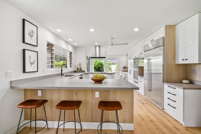 kitchen featuring kitchen peninsula, ceiling fan, appliances with stainless steel finishes, a kitchen bar, and white cabinetry