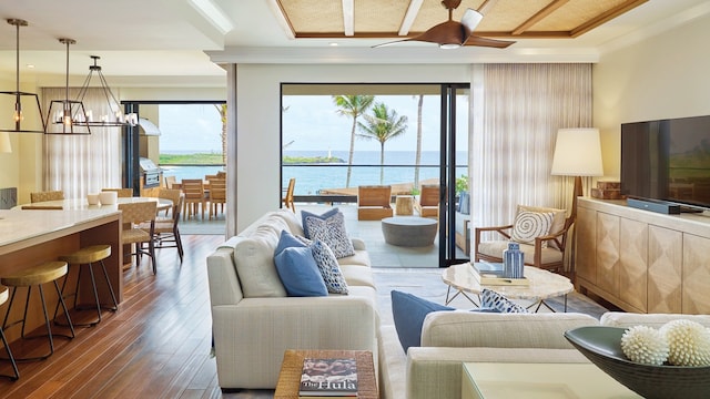 living room with ceiling fan with notable chandelier, a water view, and dark wood-type flooring