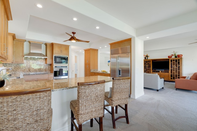 kitchen with wall chimney range hood, a kitchen breakfast bar, tasteful backsplash, kitchen peninsula, and built in appliances