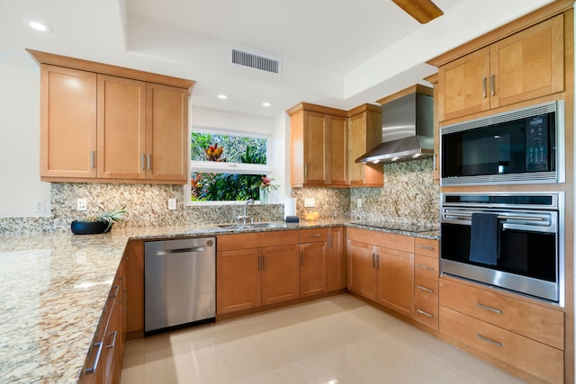 kitchen with sink, wall chimney exhaust hood, light stone countertops, tasteful backsplash, and stainless steel appliances