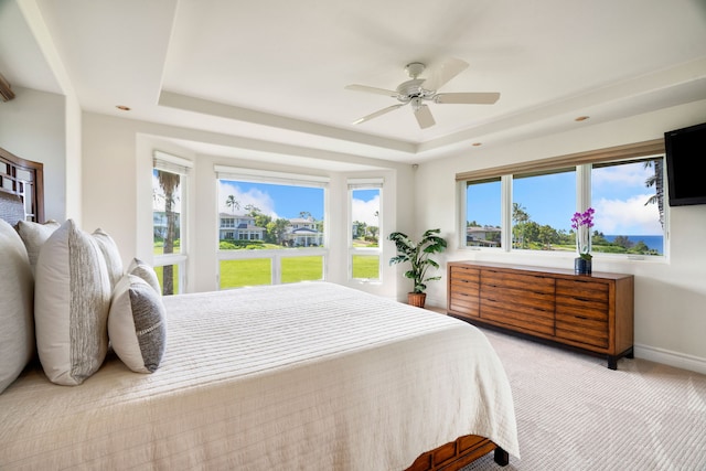 carpeted bedroom featuring multiple windows, a tray ceiling, and ceiling fan