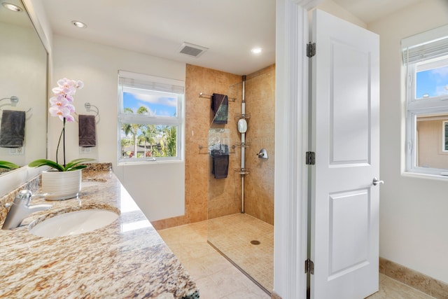 bathroom featuring tile patterned flooring, vanity, a tile shower, and a wealth of natural light