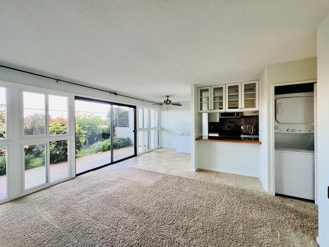 unfurnished living room featuring light tile patterned floors, a textured ceiling, ceiling fan, and stacked washer / drying machine