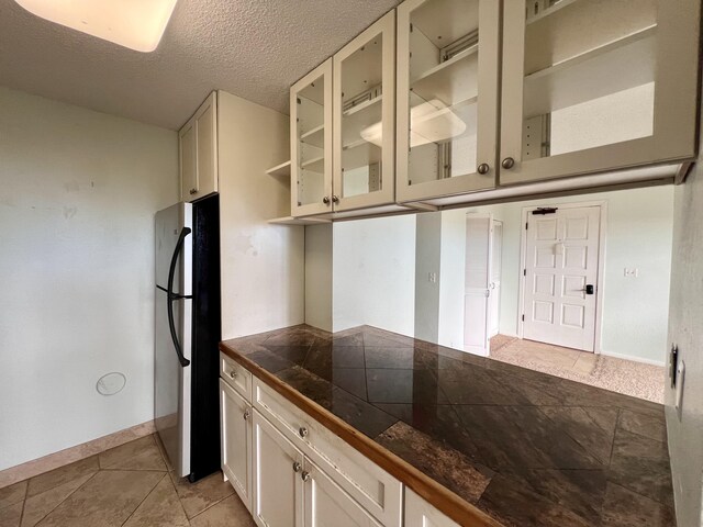 kitchen with black refrigerator, light tile patterned flooring, white cabinetry, and a textured ceiling