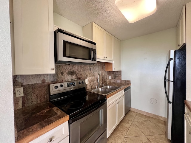 kitchen featuring decorative backsplash, stainless steel appliances, sink, light tile patterned floors, and white cabinets