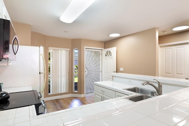 kitchen with white cabinetry, tile counters, stove, and sink