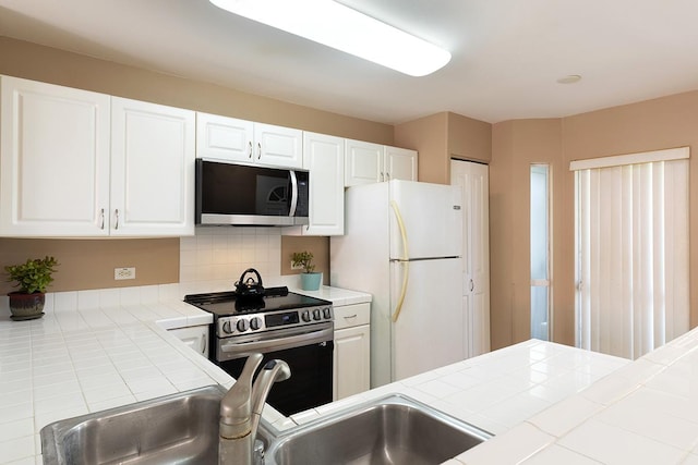 kitchen featuring backsplash, tile counters, white cabinets, and appliances with stainless steel finishes