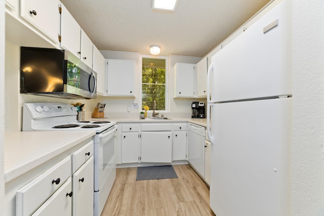 kitchen with white appliances, light wood-type flooring, a sink, and white cabinets