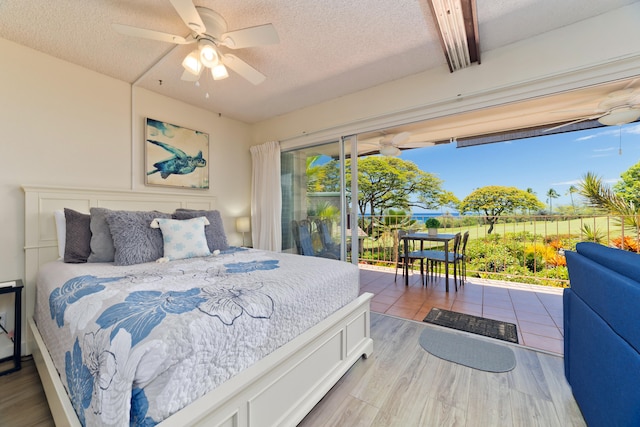 bedroom with access to exterior, light wood-type flooring, a textured ceiling, and a ceiling fan