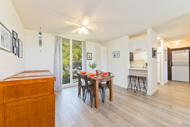 dining room featuring light wood-style floors, ceiling fan, a textured ceiling, and stacked washer and clothes dryer