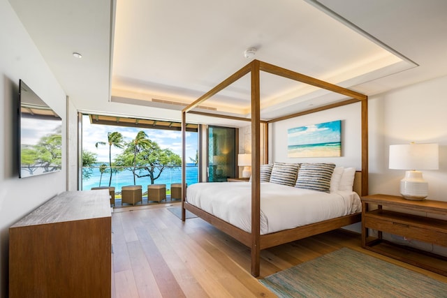 bedroom with a tray ceiling, light hardwood / wood-style flooring, and a water view