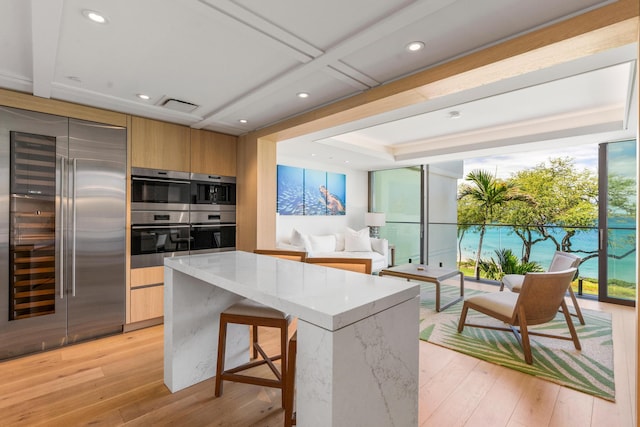 kitchen with light hardwood / wood-style flooring, a breakfast bar, stainless steel appliances, a center island, and light stone countertops