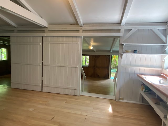 interior space with wood walls, light hardwood / wood-style floors, and vaulted ceiling with beams