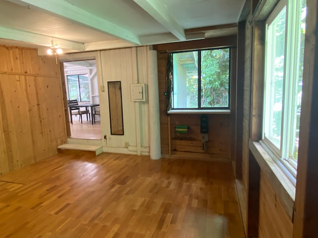 empty room featuring beamed ceiling, a wealth of natural light, wood-type flooring, and wooden walls