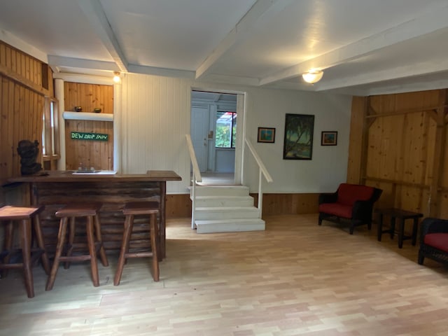 bar with wooden walls, light hardwood / wood-style flooring, and beam ceiling