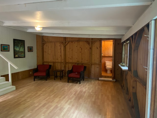 sitting room featuring wooden walls, hardwood / wood-style floors, and beam ceiling