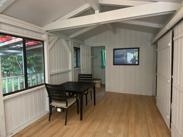 interior space featuring lofted ceiling with beams, light hardwood / wood-style flooring, and wooden walls