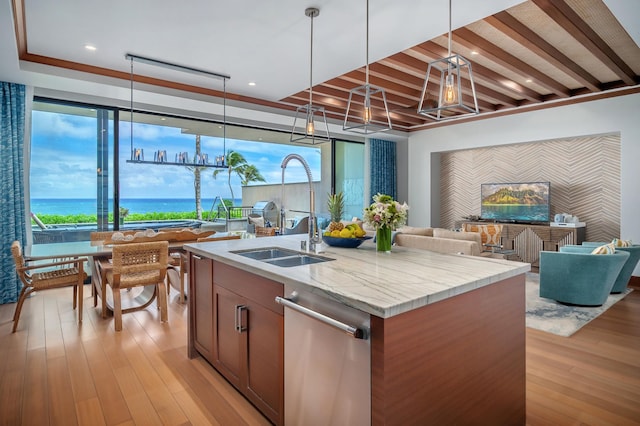 kitchen with sink, stainless steel dishwasher, an island with sink, light hardwood / wood-style floors, and light stone counters