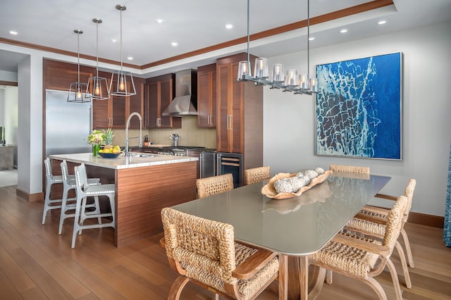 kitchen with a kitchen breakfast bar, sink, wall chimney exhaust hood, an island with sink, and decorative light fixtures