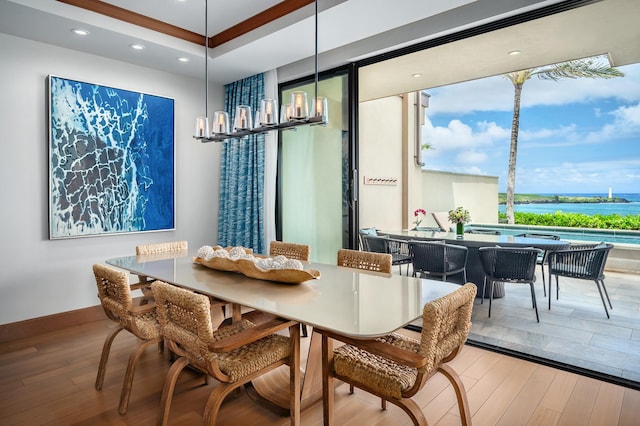 dining space featuring an inviting chandelier, a raised ceiling, crown molding, hardwood / wood-style floors, and a water view