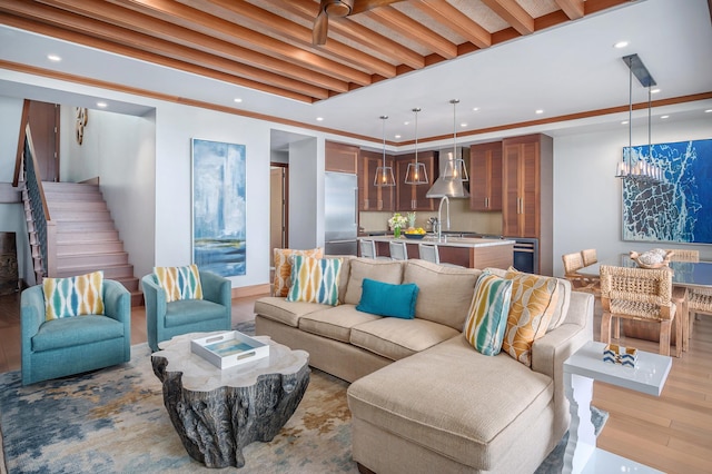 living room featuring beam ceiling, ornamental molding, sink, and light hardwood / wood-style flooring