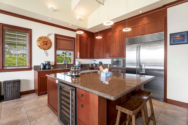 kitchen featuring beverage cooler, built in appliances, dark stone counters, decorative light fixtures, and a kitchen island