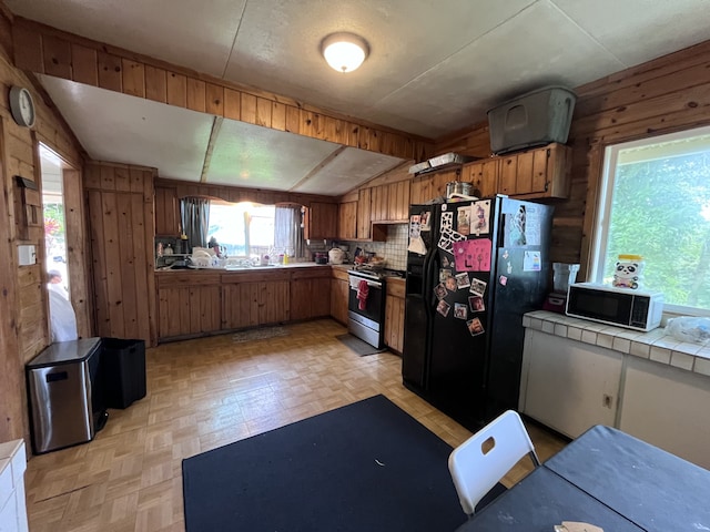 kitchen featuring wooden walls, lofted ceiling, sink, tile counters, and black appliances