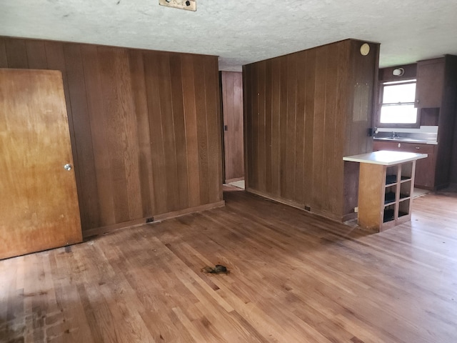 kitchen with wooden walls, kitchen peninsula, light hardwood / wood-style floors, and a textured ceiling