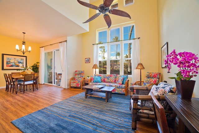 living room featuring ceiling fan with notable chandelier, hardwood / wood-style floors, and a high ceiling