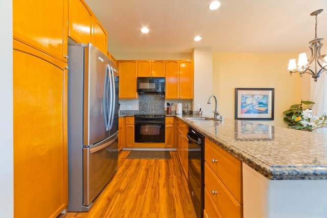 kitchen with tasteful backsplash, black appliances, sink, hanging light fixtures, and light hardwood / wood-style floors