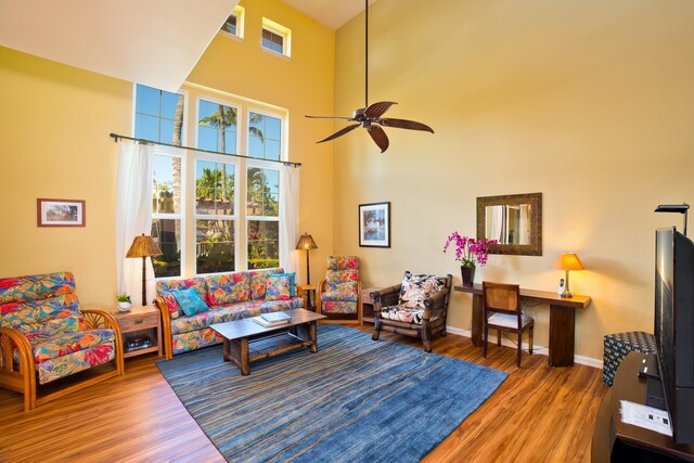 living room with a high ceiling, ceiling fan, and wood-type flooring