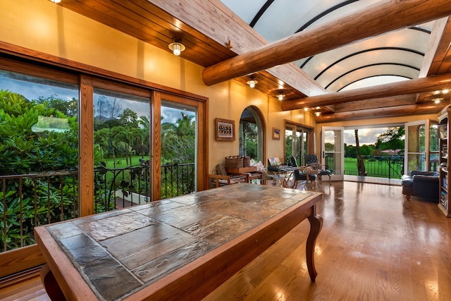 dining space with wood-type flooring, vaulted ceiling with beams, and a healthy amount of sunlight