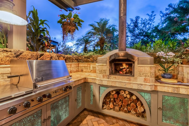 patio terrace at dusk featuring area for grilling, an outdoor stone fireplace, and a grill