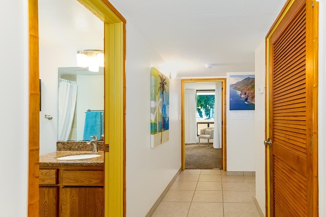 hall featuring light tile patterned floors, baseboards, and a sink