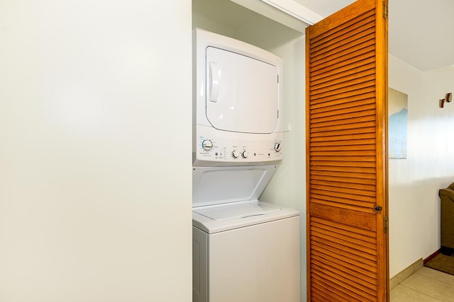 laundry area featuring light tile patterned floors, laundry area, stacked washer and clothes dryer, and baseboards