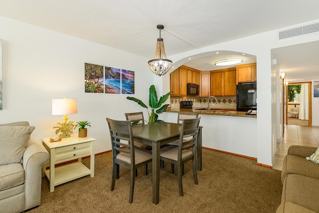 carpeted dining area featuring visible vents, baseboards, arched walkways, a notable chandelier, and a sink