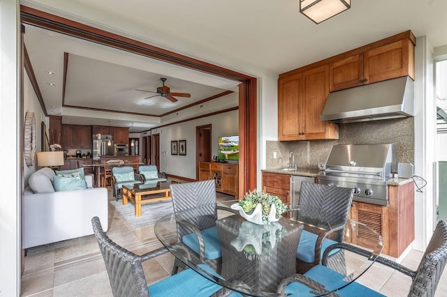 tiled dining area with ceiling fan, a raised ceiling, ornamental molding, and sink