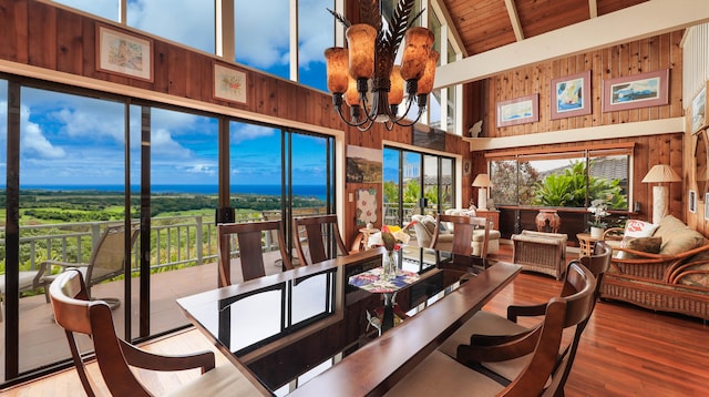 dining area featuring hardwood / wood-style flooring, a towering ceiling, a notable chandelier, and wooden walls