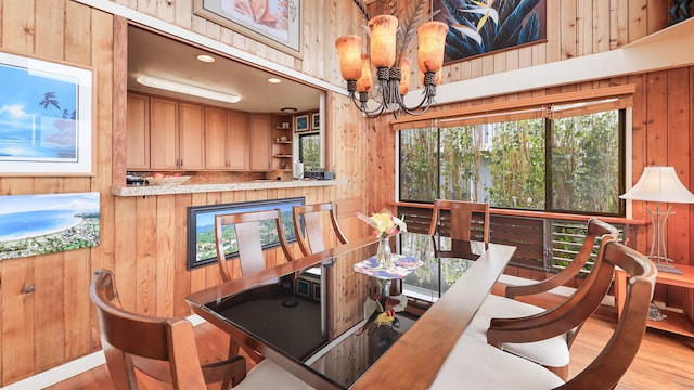 dining space featuring light hardwood / wood-style flooring, an inviting chandelier, and wooden walls