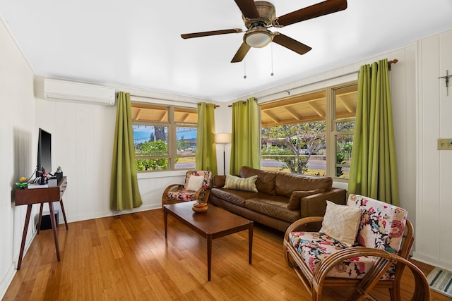 living room with a wall unit AC, light wood-type flooring, and ceiling fan