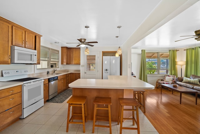 kitchen with white appliances, sink, light wood-type flooring, a kitchen breakfast bar, and ceiling fan