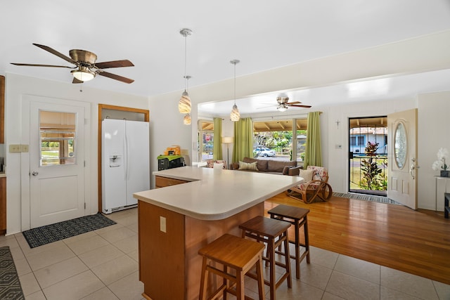 kitchen with ceiling fan, a breakfast bar, light hardwood / wood-style flooring, and white fridge with ice dispenser