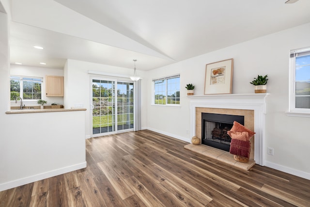 unfurnished living room featuring sink, a tile fireplace, wood-type flooring, and vaulted ceiling